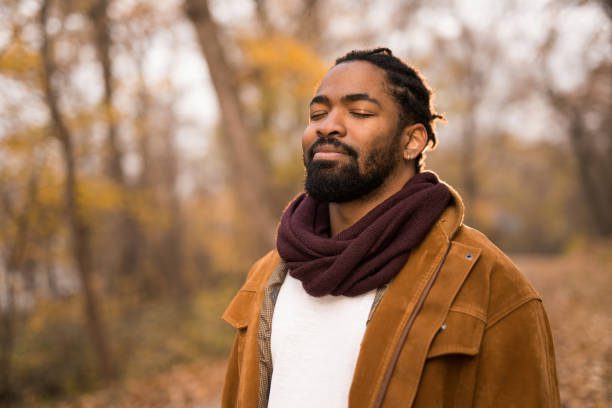 Peaceful African American man relaxing in autumn nature with eyes closed.